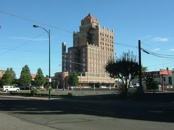 青空の下、大きな建物が建っており周りには車が停止している写真